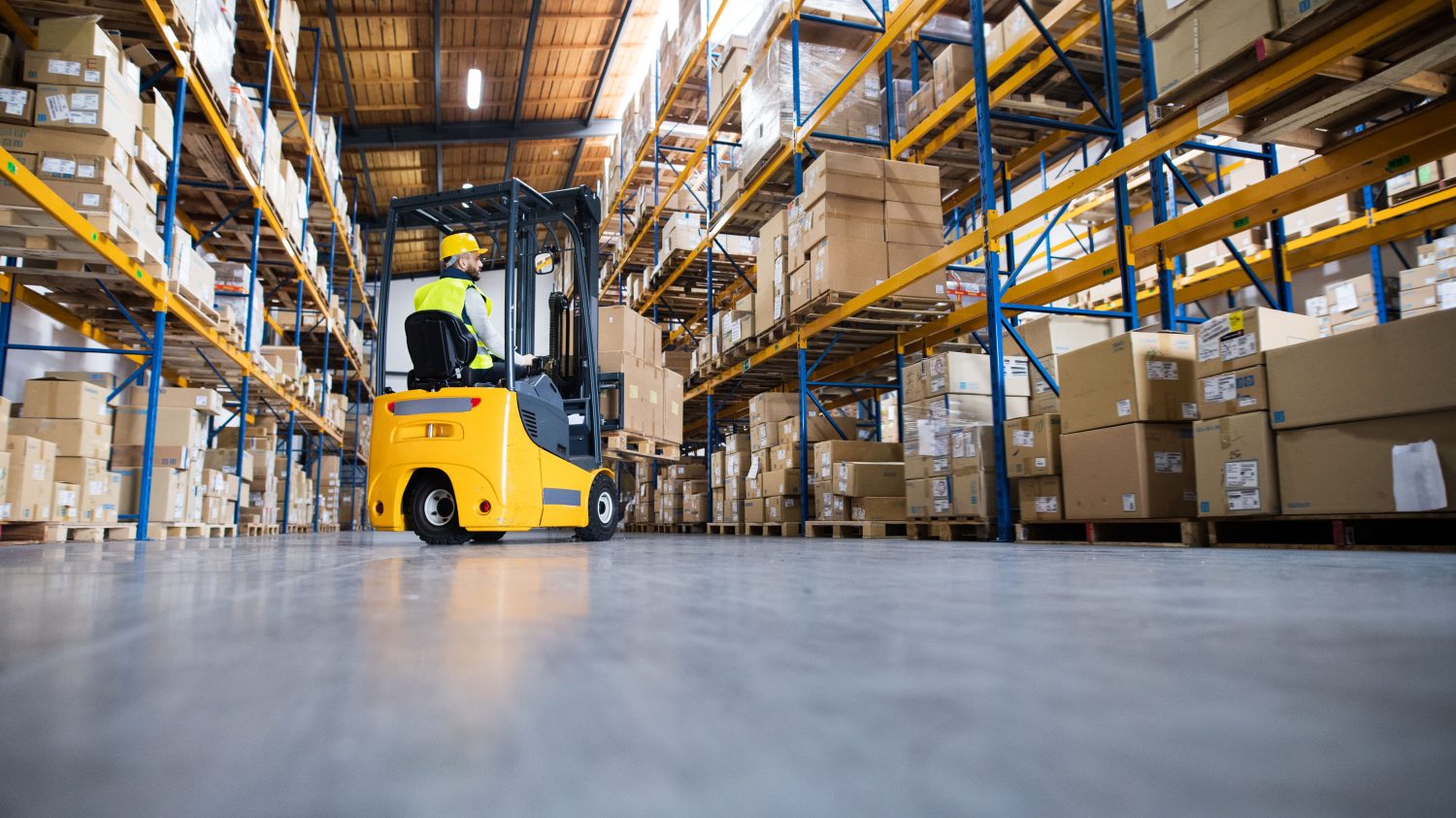 Young male worker lowering a pallet with boxes. Forklift driver working in a warehouse.